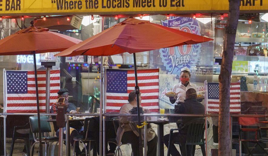In this Nov. 24, 2020, photo, a waitress serves patrons sitting outdoors for dinner separated by plastic dividers with national flags at Mel&#39;s drive-in restaurant on Sunset Boulevard in West Hollywood, Calif. California has now regained more than half of the 2.7 million jobs it lost at the start of the pandemic, state officials said Friday, June 17, 2021, a trend driven by restaurants and hotels hiring more people as the state gradually reopens its economy. (AP Photo/Damian Dovarganes) **FILE**
