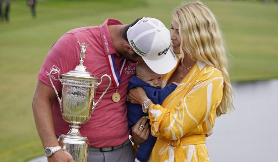 Jon Rahm, of Spain, holds the champions trophy for photographers as he stands with his wife, Kelley Rahm and kisses their child, Kepa Rahm, 11 months, after the final round of the U.S. Open Golf Championship, Sunday, June 20, 2021, at Torrey Pines Golf Course in San Diego. (AP Photo/Marcio Jose Sanchez) **FILE**
