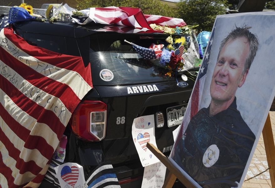 Flowers, flags and notes cover a patrol car and bike outside Arvada City Hall during a memorial for Arvada Police Officer Gordon Beesley on Tuesday, June 22, 2021 in Arvada, Colo. Officer Beesley was killed during a shooting in Olde Town Arvada. (RJ Sangosti/The Denver Post via AP)