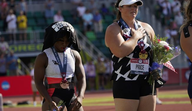 Gwendolyn Berry, left, drapes her &quot;Activist Athlete&quot; T-Shirt over her head as DeAnna Price stands for the national anthem after the finals of the women&#x27;s hammer throw at the U.S. Olympic Track and Field Trials Saturday, June 26, 2021, in Eugene, Ore. Price won and Berry finished third. (AP Photo/Charlie Riedel)