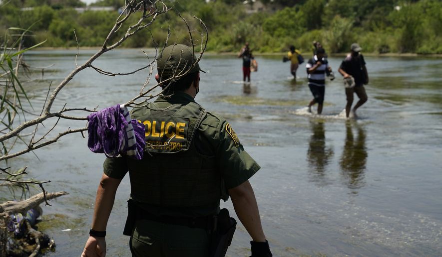A Border Patrol agent watches as a group of migrants walk across the Rio Grande on their way to turn themselves in upon crossing the U.S.-Mexico border, Tuesday, June 15, 2021, in Del Rio, Texas. U.S. government data shows that 42% of all families encountered along the border in May hailed from places other than Mexico, El Salvador, Guatemala and Honduras  the traditional drivers of migratory trends. (AP Photo/Eric Gay)
