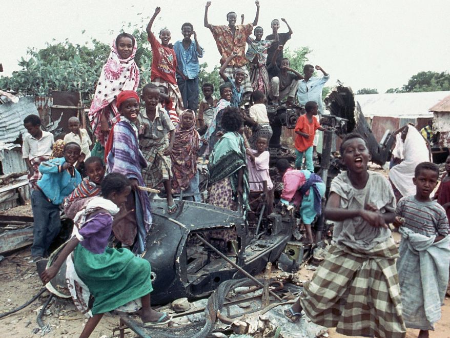 FILE - In this Oct. 19, 1993 file photo, a group of young Somalis chant anti-American slogans while sitting atop the burned out hulk of a U.S. Black Hawk helicopter, shot down during a firefight with Somali guerrillas, in Mogadishu, Somalia. In the final days of his presidency, George H.W. Bush committed the U.S. military to a mission many would later regret, ordering more than 20,000 troops into Somalia to "save thousands of innocents from death." (AP Photo/Dominique Mollard, File)