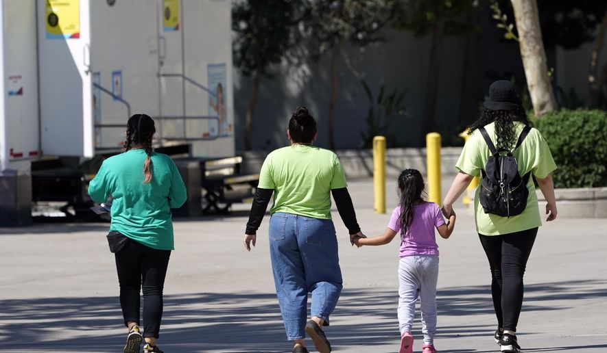 A child holds hands with workers at an emergency shelter for migrant children Friday, July 2, 2021, in Pomona, Calif. The Biden administration on Friday gave a rare look inside an emergency shelter it opened to house migrant children crossing the U.S.-Mexico border alone, calling the California facility a model among its large-scale sites, some of which have been plagued by complaints. (AP Photo/Marcio Jose Sanchez, Pool)