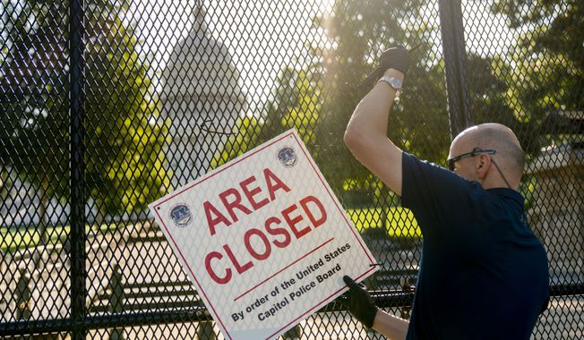 A worker with the U.S. Capitol Police takes down signs that read &quot;Area Closed&quot; on fencing surrounding the U.S. Capitol Building erected following the Jan. 6 riot at the Capitol, Friday, July 9, 2021, in Washington. The fencing will be taken down soon. (AP Photo/Andrew Harnik)