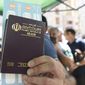 A person holds up an Iranian passport as people, most of them residents of Iran stand in line for a vaccine at a mobile vaccination station in the center of Yerevan , Armenia, Friday, July 9, 2021. Armenia’s offer of free coronavirus vaccines to any foreign visitor has drawn many people from neighboring Iran and other countries to the ex-Soviet Caucasus nation. The Iranians initially visited the Armenian border city of Meghri to get the shots, but the Armenian authorities have decided earlier this week that all foreign nationals should get the shots in the Armenian capital, Yerevan. (Lusi Sargsyan/PHOTOLURE via AP)