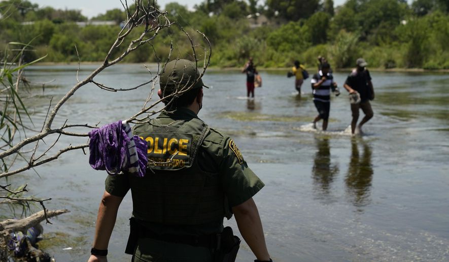 In this June 15, 2021, photo, a Border Patrol agent watches as a group of migrants walk across the Rio Grande on their way to turning themselves in upon crossing the U.S.-Mexico border in Del Rio, Texas. (AP Photo/Eric Gay) **FILE**