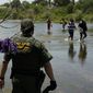 In this June 15, 2021, photo, a Border Patrol agent watches as a group of migrants walk across the Rio Grande on their way to turning themselves in upon crossing the U.S.-Mexico border in Del Rio, Texas. (AP Photo/Eric Gay) **FILE**