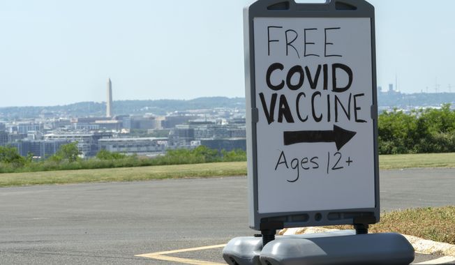 In this Wednesday, May 19, 2021, file photo, downtown Washington and the Washington Monument are seen behind a sign adverting a free vaccine drive with Pfizer COVID-19 vaccinations for members of the community 12 years and up outside a school in southeast Washington.  (AP Photo/Jacquelyn Martin, File)  **FILE**
