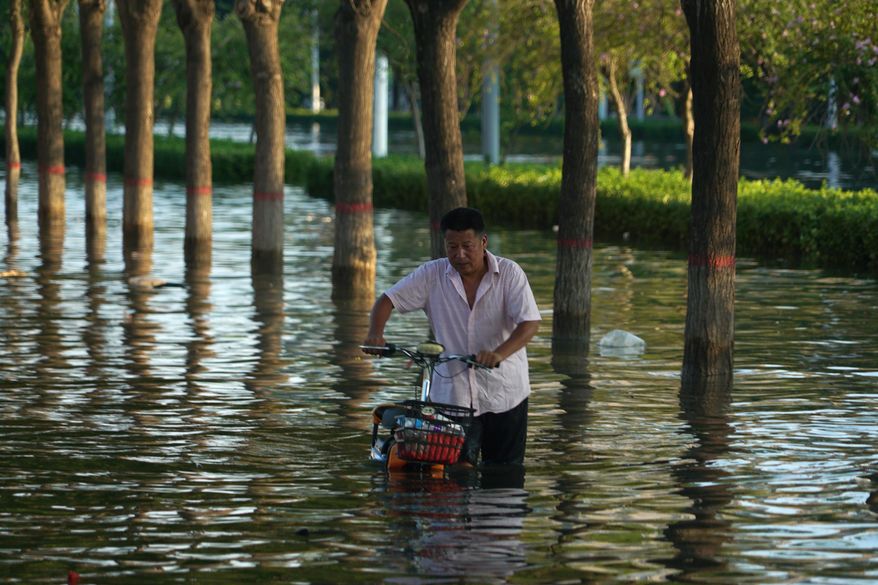 In this July 26, 2021, file photo, a man pushes a scooter through floodwaters in Xinxiang in central China's Henan Province. Chinese authorities have announced a huge jump in the death toll from recent floods. The Henan province government said Monday, Aug. 2, 2021, that over 300 have people died and at least 50 remain missing. (AP Photo/Dake Kang, File)