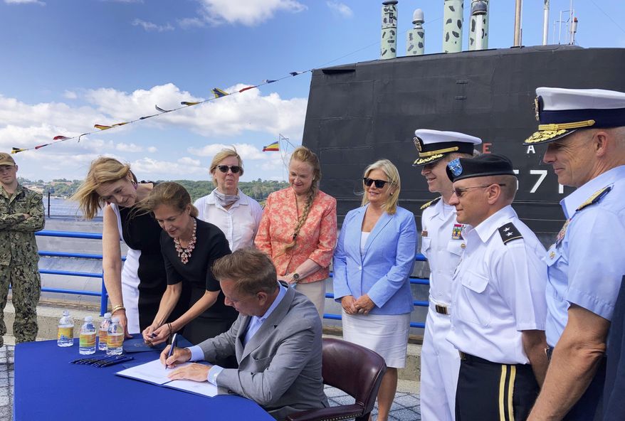Connecticut Gov. Ned Lamont signs copies of a bill concerning military spouses. Monday, Aug. 2, 2021, at the Submarine Force Museum in Groton, Conn. The law, which takes effect Oct. 1, makes it easier for spouses of active duty military personnel to obtain state occupational licenses. Some have had to wait months, if not years, to get their license from another state recognized by Connecticut. Standing next to Lamont at the table is Lt. Gov. Susan Bysiewicz. Also attending are state legislators from southeastern Connecticut, and military officers assigned to the U.S. Submarine Base, New London, including Capt. Todd Moore, third from right, commanding officer at the base. (AP Photo/Susan Haigh)