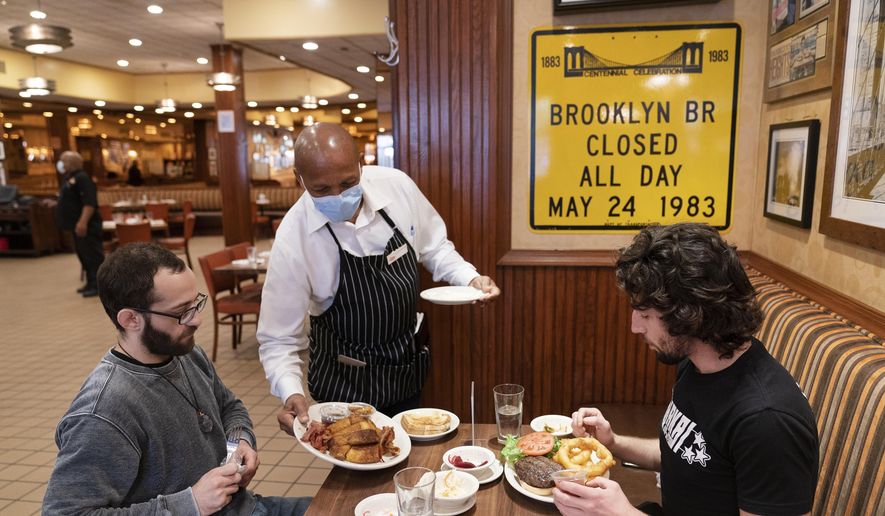 In this Sept. 30, 2020, file photo, Waiter Lenworth Thompson serves lunch to David Zennario, left, and Alex Ecklin at Junior&#x27;s Restaurant in New York. New York City will soon require proof of COVID-19 vaccinations for anyone who wants to dine indoors at a restaurant, see a performance or go to the gym, Mayor Bill de Blasio announced Tuesday, Aug. 3, making it the first big city in the U.S. to impose such restrictions. (AP Photo/Mark Lennihan, File)