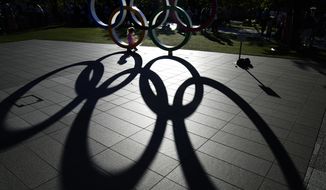 A child sits in the Olympic rings on display outside the Olympic Stadium where the athletic events are underway at the 2020 Summer Olympics, Tuesday, Aug. 3, 2021, in Tokyo. (AP Photo/David Goldman)