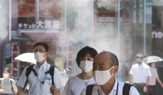 People wearing face masks to protect against the spread of the coronavirus walk under a water mist in Tokyo Thursday, Aug. 5, 2021. New cases surge in Tokyo to record levels during the Olympic Games. (AP Photo/Koji Sasahara)