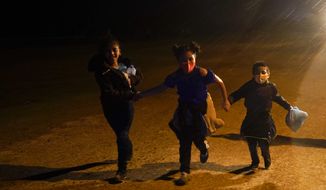 In this May 11, 2021, photo, three young migrants hold hands as they run in the rain at an intake area after turning themselves in upon crossing the U.S.-Mexico border in Roma, Texas. An official says the Biden administration has begun flying some Central American families deep into Mexico as authorities encounter more families and unaccompanied children at the U.S.-Mexico border. (AP Photo/Gregory Bull) **FILE**