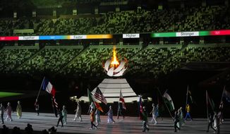The Olympic flame burns as athletes and volunteers carry flags during the closing ceremony in the Olympic Stadium at the 2020 Summer Olympics, Sunday, Aug. 8, 2021, in Tokyo, Japan. (AP Photo/Vincent Thian)