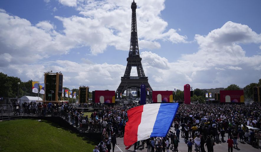 A man unfurls a French flag at the Olympics fan zone at Trocadero Gardens in front of the Eiffel Tower in Paris, Sunday, Aug. 8, 2021. A giant flag will be unfurled on the Eiffel Tower in Paris Sunday as part of the handover ceremony of Tokyo 2020 to Paris 2024, as Paris will be the next Summer Games host in 2024. The passing of the hosting baton will be split between the Olympic Stadium in Tokyo and a public party and concert in Paris. (AP Photo/Francois Mori) **FILE**