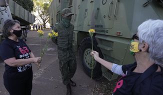 Women offer flowers to a soldier in a show of opposition to Brazilian President Jair Bolsonaro after a military convoy passed Planalto presidential palace and parked outside the Navy headquarters in Brasilia, Brazil, Tuesday, Aug. 10, 2021. The convoy paraded by the palace on Tuesday, the day of a key congressional vote on a constitutional reform proposal supported by Bolsonaro that would add printed receipts to some of the nation’s electronic ballot boxes. (AP Photo/Eraldo Peres)