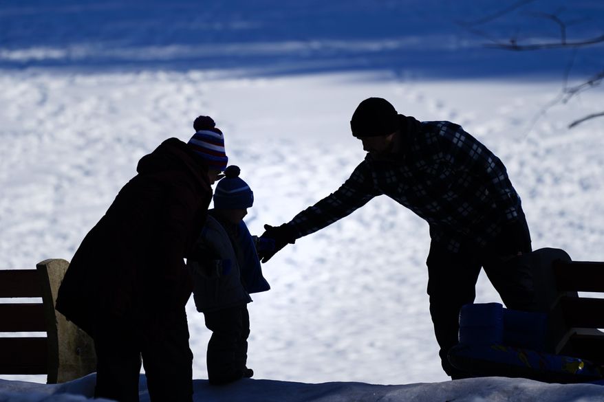 In this Feb. 5, 2021 file photo, a couple helps a child on a snow-covered embankment in Huntingdon Valley, Pa. (AP Photo/Matt Rourke)