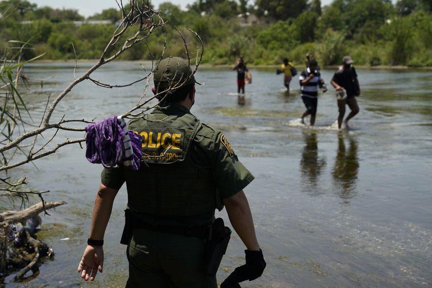 In this June 15, 2021, file photo a Border Patrol agent watches as a group of migrants walk across the Rio Grande on their way to turn themselves in upon crossing the U.S.-Mexico border in Del Rio, Texas. (AP Photo/Eric Gay, File)