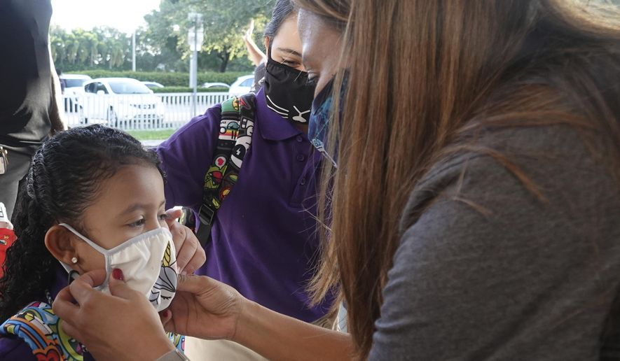 Dolphin Bay Elementary School kindergarten student Isabela Osorio gets an assist with her mask from her sister Valentina and Assistant Principal Janet Blano Soto, Wednesday, Aug. 16, 2021, in Miramar, Fla. More than 261,000 Broward County Public Schools (BCPS) students headed back to school to begin the 2021/22 school year. (Joe Cavaretta/South Florida Sun-Sentinel via AP)