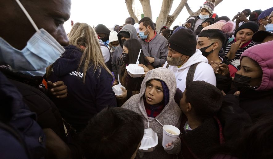 In this Friday, Feb. 19, 2021, file photo, asylum seekers receive food as they wait for news of policy changes at the border, in Tijuana, Mexico. (AP Photo/Gregory Bull, File)