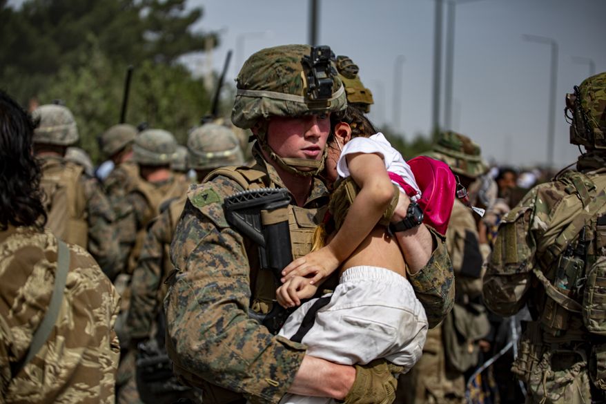 In this Aug. 20, 2021, photo provided by the U.S. Marine Corps, a Marine assigned to the 24th Marine Expeditionary Unit carries a girl at a gate to Hamid Karzai International Airport in Kabul, Afghanistan. (1st Lt. Mark Andries/U.S. Marine Corps via AP)