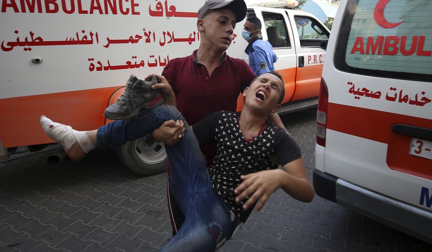 A protestor helps a wounded youth, who was shot by Israeli troops in his foot during a protest at the Gaza Strip&#39;s border with Israel, into the treatment room of Shifa hospital in Gaza City, Saturday, Aug. 21, 2021. (AP Photo/Abdel Kareem Hana)