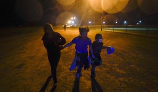 In this May 11, 2021, file photo, three young migrants hold hands as they run in the rain at an intake area after turning themselves in upon crossing the U.S.-Mexico border in Roma, Texas. Five months after the Biden administration declared an emergency and raced to set up shelters to house a record number of children crossing the U.S.-Mexico border alone, kids continue to languish at the sites, while more keep coming, child welfare advocates say. (AP Photo/Gregory Bull) ** FILE **