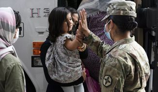 In this Monday, Aug. 30, 2021, file photo, Army Pfc. Kimberly Hernandez gives a high-five to a girl evacuated from Kabul, Afghanistan, before boarding a bus after they arrived at Washington Dulles International Airport, in Chantilly, Va. U.S. religious groups of many faiths are gearing up to assist the thousands of incoming refugees. (AP Photo/Jose Luis Magana, File)