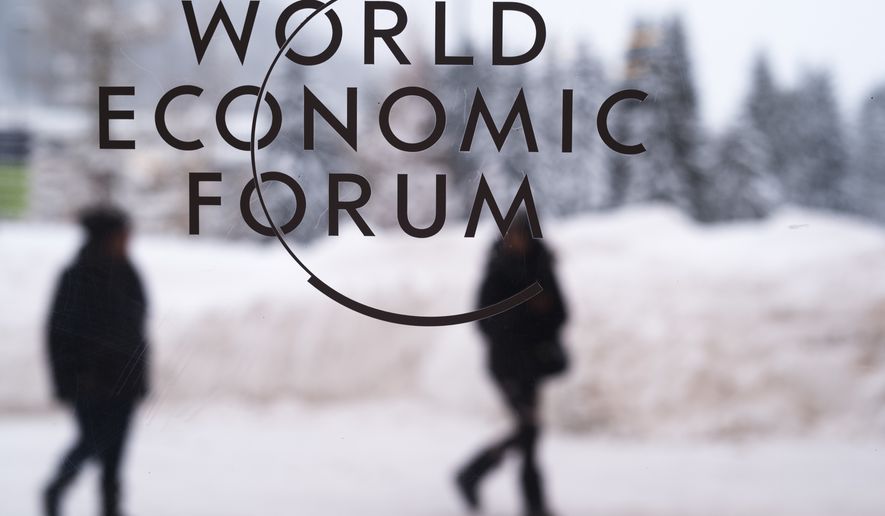 In this Sunday, Jan. 21, 2018, file photo, two people walk behind the logo of the World Economic Forum at the meeting&#x27;s conference center in Davos, Switzerland. (AP Photo/Markus Schreiber, file)
