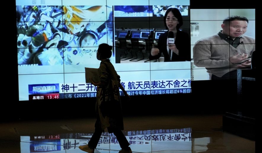 A woman walks by a TV screen showing CCTV broadcasting a news of Chinese astronauts sit inside the Shenzhou-12 manned spacecraft preparing to return to earth, at a shopping mall in Beijing, Thursday, Sept. 16, 2021. (AP Photo/Andy Wong)