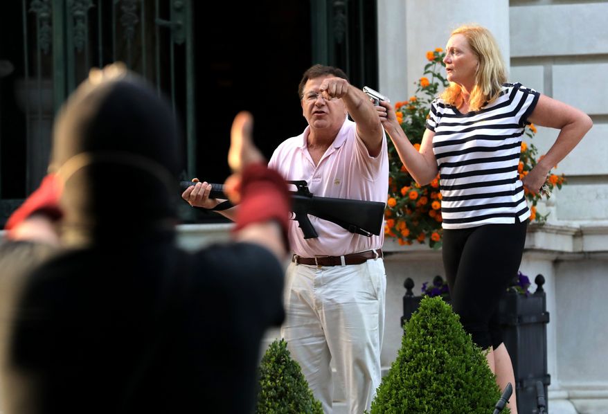 In this June 28, 2020, file photo, armed homeowners Mark and Patricia McCloskey, standing in front of their house along Portland Place, confront protesters marching to St. Louis Mayor Lyda Krewson&#39;s house in the Central West End of St. Louis. (Laurie Skrivan/St. Louis Post-Dispatch via AP) ** FILE **