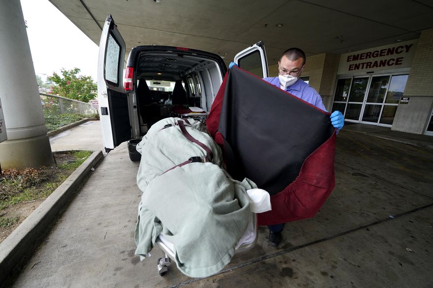 In this Aug. 18, 2021, file photo, an employee of a local funeral home covers the body of a COVID-19 patient who died as he prepares to take it away from a loading dock, at the Willis-Knighton Medical Center in Shreveport, La. (AP Photo/Gerald Herbert, File)