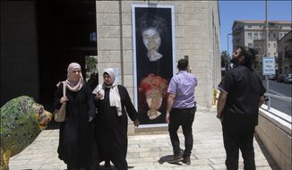 In this July 1, 2021, file photo provided by the The Lonka Project, people look at the defaced portrait of Holocaust survivor Peggy Parnass, outside Jerusalem City Hall, where it is on display as part of an exhibit that tells the stories of 400 survivors of the Nazi atrocities during World War II in The Lonka Project exhibition in Safra Square in Jerusalem. Israel is having a difficult time keeping images of women in public from being defaced. (Jim Hollander/The Lonka Project via AP) ** FILE **