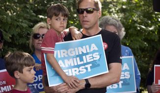 Patrick Novecosky, of Warrenton, Va., holds his son Daniel, 7, and son Peter, 9 stands beside them, as they participate in a rally sponsored by Catholic Vote and Fight for Schools, in Leesburg, Va., Saturday, Oct. 2, 2021. When Democrat Terry McAuliffe said during the Virginia governor’s debate last week that he doesn’t believe “parents should be telling schools what they should teach,” his opponent pounced. Republican Glenn Youngkin quickly turned the footage into a digital ad, then announced spending $1 million on a commercial airing statewide proclaiming that “Terry went on the attack against parents.” (AP Photo/Cliff Owen)