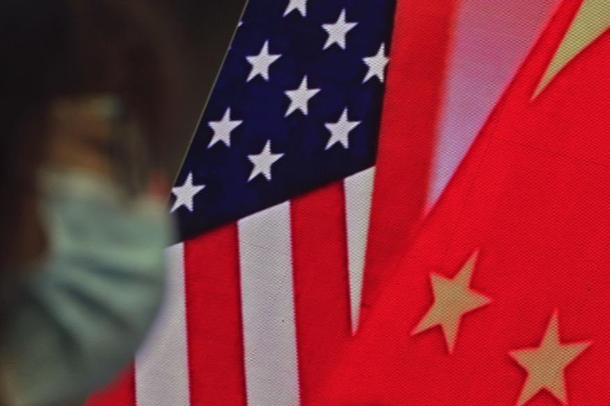 In this Feb. 22, 2021, file photo, a woman wearing a face mask sits near a screen showing China and U.S. flags as she listens to a speech by Chinese Foreign Minister Wang Yi at the Lanting Forum on bringing China-U.S. relations back to the right track, at the Ministry of Foreign Affairs office in Beijing. (AP Photo/Andy Wong, File)