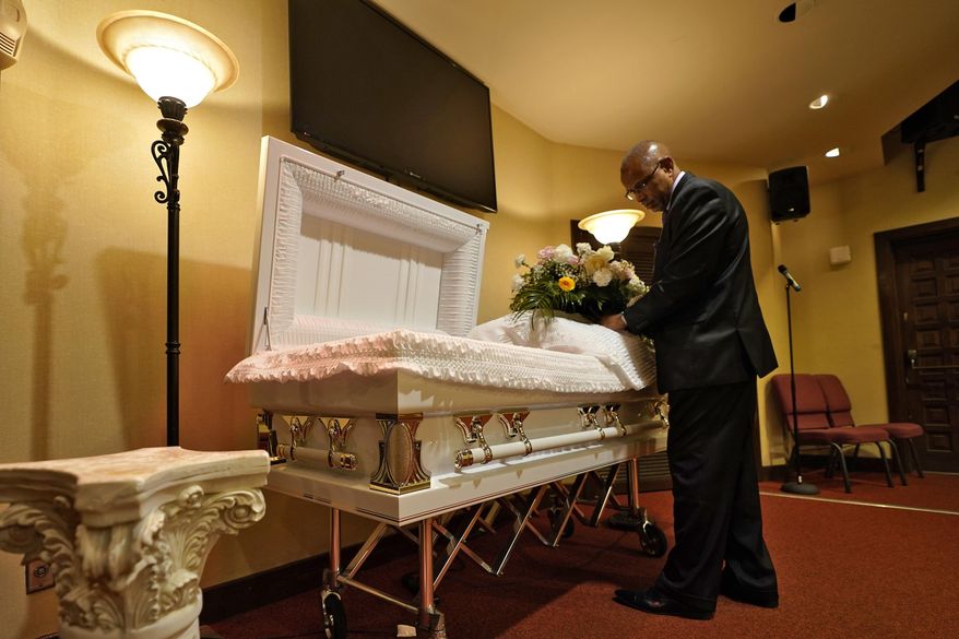 In this Thursday, Sept. 2, 2021, file photo, a funeral director arranges flowers on a casket before a service in Tampa, Fla. According to a study published Thursday, Oct. 7, 2021, by the medical journal Pediatrics, the number of U.S. children orphaned during the COVID-19 pandemic may be larger than previously estimated, and the toll has been far greater among Black and Hispanic Americans. (AP Photo/Chris O&#39;Meara, File)