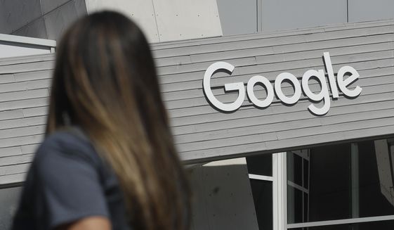 In this Sept. 24, 2019, photo, a woman walks below a Google sign on the campus in Mountain View, Calif.  Google on Thursday, Oct. 7, 2021, will no longer allow digital ads promoting false climate change claims to appear next to the content of other publishers, hoping to deny money to those making such claims and to stop the spread of misinformation on its platform. (AP Photo/Jeff Chiu) **FILE**
