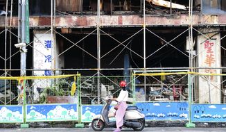A woman stops to look at the burnt building in Kaohsiung in southern Taiwan on Friday, Oct. 15, 2021. Dozens were killed and dozens more injured after a fire broke out early Thursday in a decades-old mixed commercial and residential building in the Taiwanese port city of Kaohsiung, officials said. (AP Photo/Huizhong Wu)