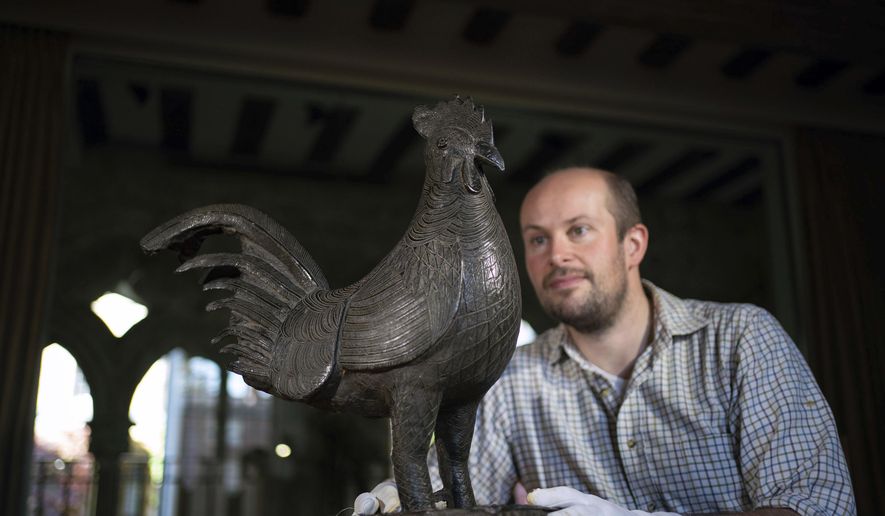 Archivist Robert Athol looks at a bronze statue of a cockerel called The Okukor, one of the Benin Bronzes, at Jesus College, University of Cambridge, England, Friday Oct. 15, 2021. The Cambridge University college will return a looted bronze cockerel to Nigeria later this month, making it the first U.K. institution to hand back one of the artifacts known as the Benin Bronzes. (Joe Giddens/PA via AP)