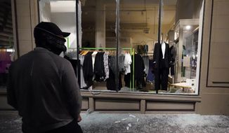 In this Nov. 4, 2020, file photo, a man stands in front of a broken display window at a retail store during protests in Portland, Ore. Police in Portland say they believe a new state law prohibits officers from directly intervening when people smash storefronts and cause mayhem. The measure passed this year prohibits the use of crowd control methods like pepper spray and rubber bullets &quot;unless use of force is otherwise authorized by statute.&quot; (AP Photo/Marcio Jose Sanchez, File)