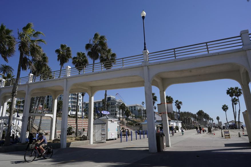 A man bikes under a bridge connecting the Oceanside pier to Pacific Street Friday, Oct. 15, 2021, in Oceanside, Calif. The iconic bridge is deteriorating because the city lacks the money for a roughly $25 million rehabilitation. One reason the project has slowed while projects in other cities are moving ahead revolves around the American Rescue Plan — the sweeping COVID-19 relief law championed by President Joe Biden and congressional Democrats that is pumping billions of dollars to states and local governments. (AP Photo/Gregory Bull) **FILE**