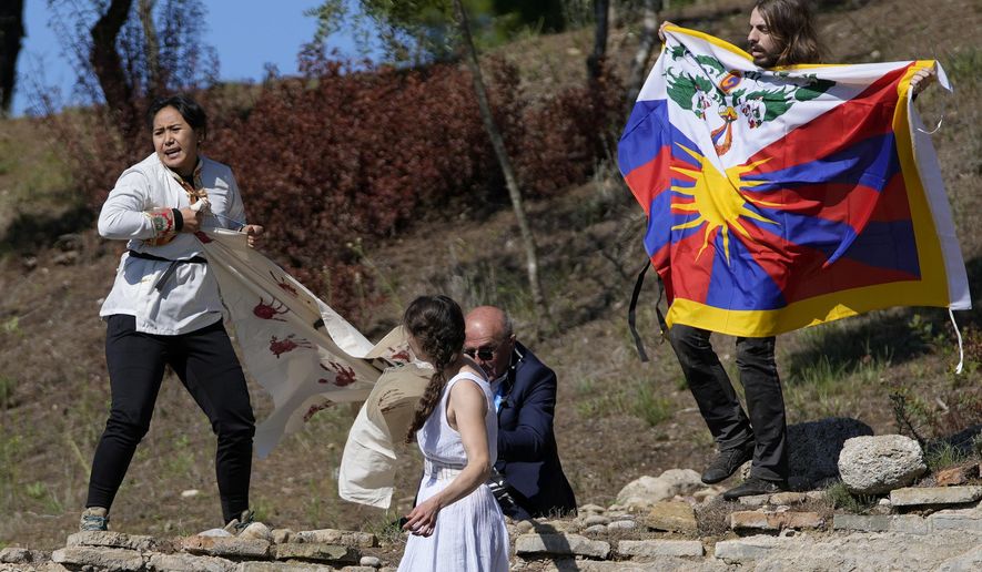 A police officer tries to stop protesters displaying a Tibetan flag and a banner reading &amp;quot;No genocide games&amp;quot; during the lighting of the Olympic flame at Ancient Olympia site, birthplace of the ancient Olympics in southwestern Greece, Monday, Oct. 18, 2021. The flame will be transported by torch relay to Beijing, China, which will host the Feb. 4-20, 2022 Winter Olympics. (AP Photo/Thanassis Stavrakis)