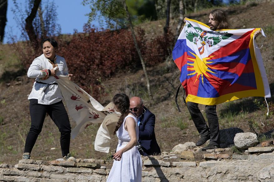 A police officer tries to stop protesters displaying a Tibetan flag and a banner reading &amp;quot;No genocide games&amp;quot; during the lighting of the Olympic flame at Ancient Olympia site, birthplace of the ancient Olympics in southwestern Greece, Monday, Oct. 18, 2021. The flame will be transported by torch relay to Beijing, China, which will host the Feb. 4-20, 2022 Winter Olympics. (AP Photo/Thanassis Stavrakis)