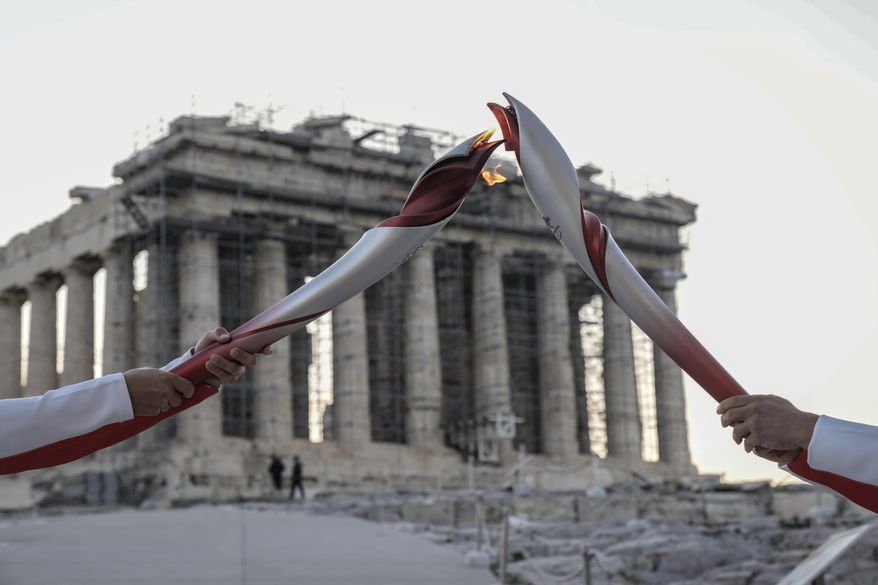 Greek torch bearer Ioannis Melissanidis, left, Olympic gold medalist in Gymnastics, passes the flame to Christos Volikakis, world Champion in Cycling, in front of the ancient Parthenon temple atop of the Acropolis Hill in Athens, Tuesday, Oct. 19, 2021. The flame will be transported by torch relay to Beijing, China, which will host the Feb. 4-20, 2022, Winter Olympics.(AP Photo/Petros Giannakouris)
