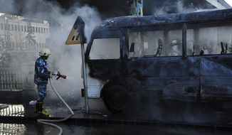 In this photo released by the Syrian official news agency SANA, a Syrian firefighter extinguishes a burned bus at the site of a deadly explosion, in Damascus, Syria, Wednesday, Oct. 20, 2021. Two roadside bombs exploded near a bus carrying troops during the morning rush hour in the Syrian capital early Wednesday, killing and wounding several people, state TV reported. (SANA via AP)