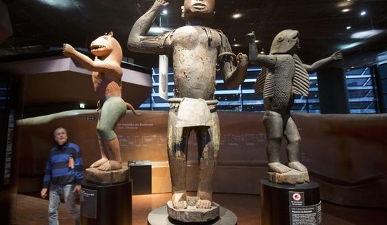 In this Friday, Nov. 23, 2018 file photo a visitor looks at wooden royal statues of the Dahomey kingdom, dated 19th century, at Quai Branly museum in Paris, France. In a decision with potential ramifications across European museums, France is displaying 26 looted colonial-era artifacts for one last time before returning them home to Benin. (AP Photo/Michel Euler, File)