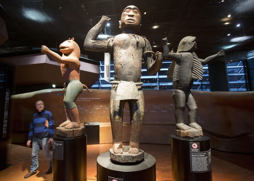 In this Friday, Nov. 23, 2018 file photo a visitor looks at wooden royal statues of the Dahomey kingdom, dated 19th century, at Quai Branly museum in Paris, France. In a decision with potential ramifications across European museums, France is displaying 26 looted colonial-era artifacts for one last time before returning them home to Benin. (AP Photo/Michel Euler, File)