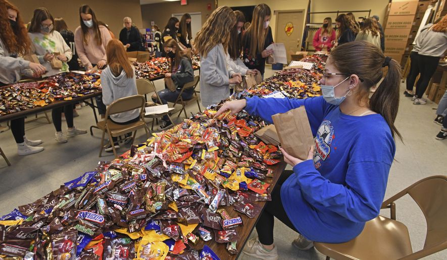In this file photo, a high school student bags candy at the Richland Township Police Department in Johnstown, Pa., Wednesday, Oct. 27, 2021, for their Trick or Treat night to be held the next day.  (John Rucosky/The Tribune-Democrat via AP)  **FILE**