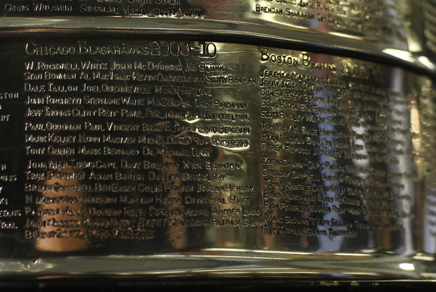 FILE - The names of the 2010 Stanley Cup Champion Chicago Blackhawks, left, are displayed on the Stanley Cup in the lobby of the United Center during an NHL hockey news conference on June 11, 2013 in Chicago. The first game of the Stanley Cup final series is Wednesday in Chicago. Blackhawks owner Rocky Wirtz wants the Hockey Hall of Fame to cover the name of an assistant coach engraved on the Stanley Cup after the assistant was accused of sexually assaulting a player during the team&#39;s run to the 2010 championship. (AP Photo/Charles Rex Arbogast, File)
